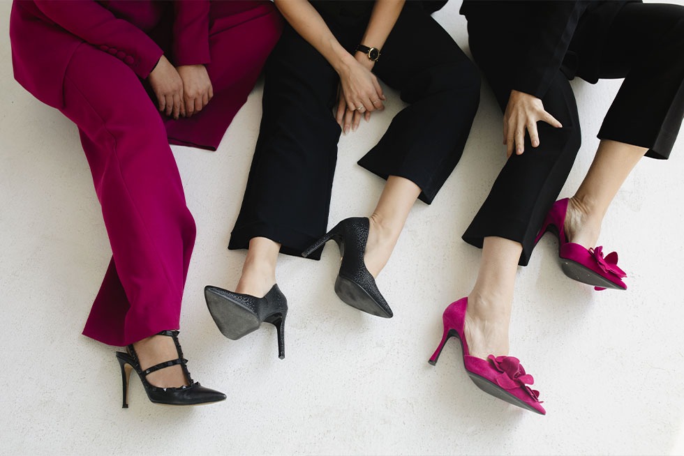 Three women seated side by side, one pair of hot pink heels among them
